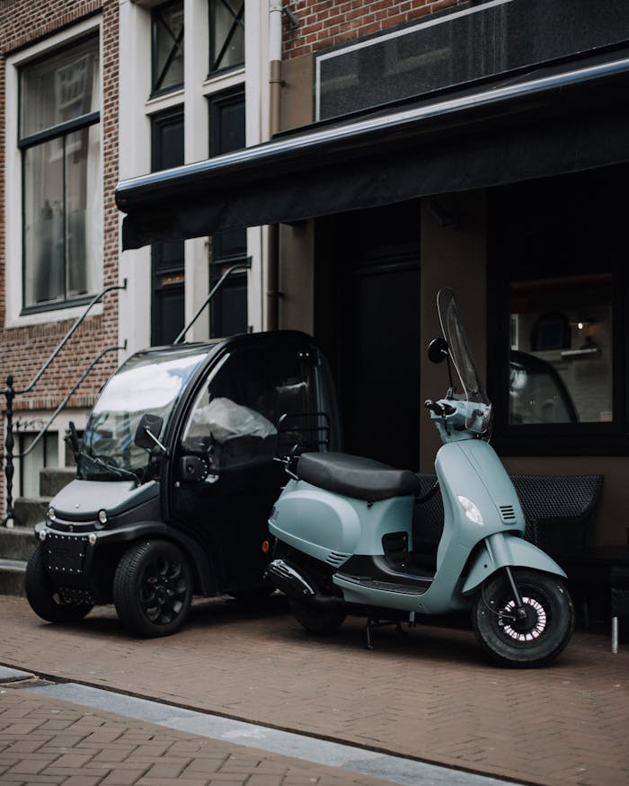 electric-mini-car-and-blue-scooter-parked-outside-a-house-5066358 A mini electronic car and vintage scooter parked in an urban city setting with brick architecture.