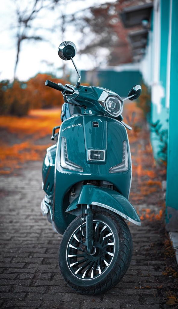 vibrant-blue-scooter-on-autumn-path-29311991 Blue retro scooter parked next to a teal wall during autumn in Yalova, Türkiye.